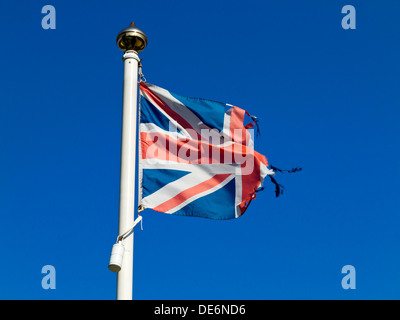 Torn British Union Jack flag on a flagpole with blue sky behind Stock Photo
