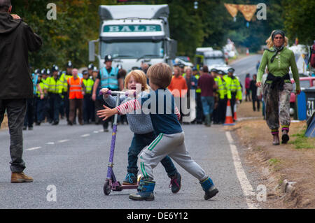 Balcombe,West Sussex, UK. 12th Sept, 2013. Children play as in the background a lorry is escorted to Cuadrilla site by Police as environmentalists walk in front... The anti fracking environmentalists are protesting against test drilling by Cuadrilla on the site in West Sussex that could lead to the controversial fracking process. Credit:  David Burr/Alamy Live News Stock Photo