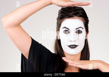 Woman made up in white face frames her features with her hands Stock Photo