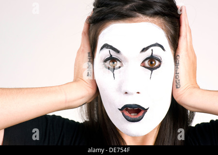 Woman made up in white face frames her features with her hands Stock Photo