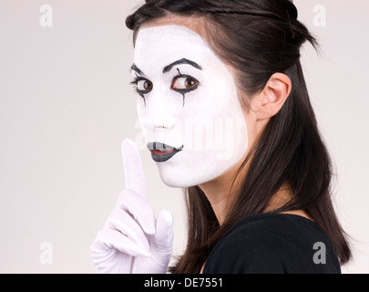 Woman made up in white face frames mouth with index finger Stock Photo