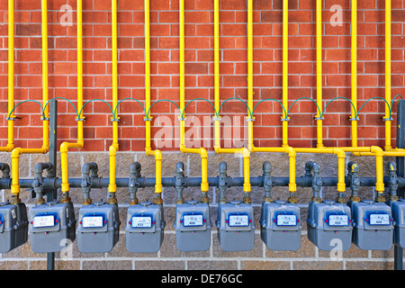 Row of natural gas meters with yellow pipes on building brick wall Stock Photo
