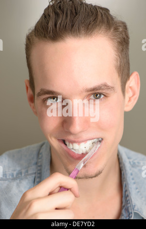 Lifestyle portrait of happy young man brushing his teeth with a pink toothbrush Stock Photo