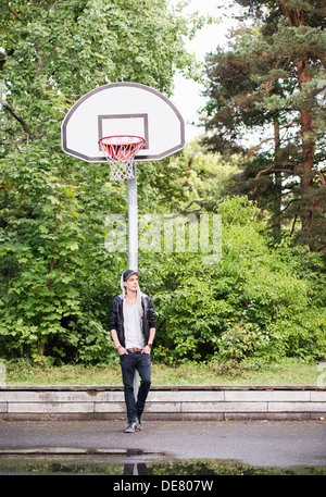 Lifestyle portrait of young man in leather jacket waiting at an outdoor basketball court Stock Photo