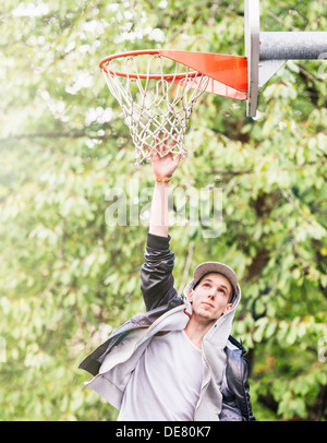 Lifestyle portrait of young man in leather jacket jumping and reching for a basketball hoop Stock Photo