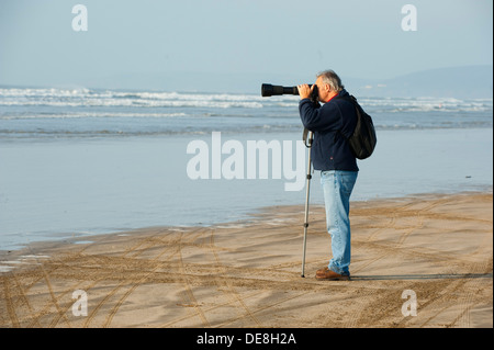Photographer taking picture using a monopod on the beach at Westward Ho! Devon, England, UK Stock Photo