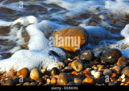 Incoming tide laps around rocks on the shingle beach at Sidmouth, Devon on the Jurassic Coast. Stock Photo