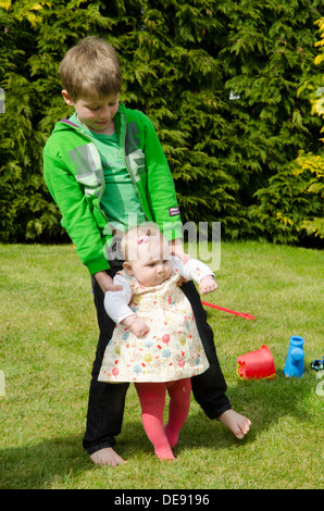 siblings eight year old boy with eight month old sister playing in garden Stock Photo