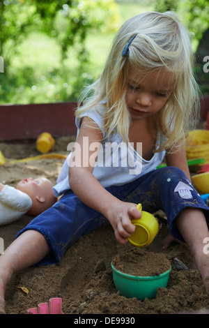 Little blond girl playing in sandpit at summer garden Stock Photo