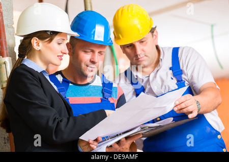 Construction site team or architect and builder or worker with helmets controlling or having discussion of plan or blueprint Stock Photo