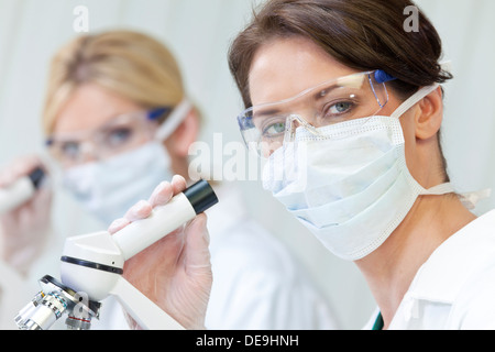 Woman medical or scientific researcher or doctor using her microscope in a laboratory with her female colleague Stock Photo