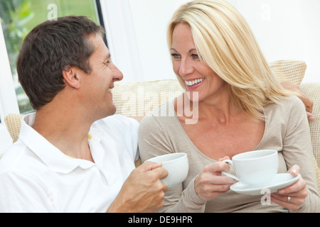 happy middle aged man and woman couple in their forties, sitting together at home on a sofa enjoying a cup of tea or coffee Stock Photo