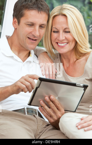 successful and happy middle aged man and woman couple in their forties, sitting together at home on a sofa using tablet computer Stock Photo