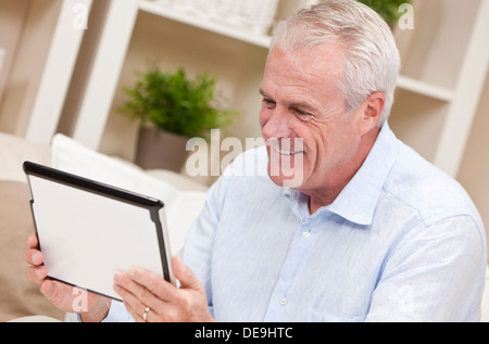 Smiling senior man at home sitting on sofa or settee using her tablet computer. Stock Photo
