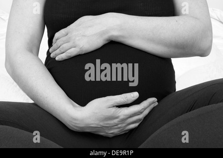 Black and white cropped shot of a pregnant woman with her hands around her unborn baby bump Stock Photo