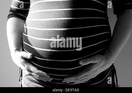 Black and white cropped shot of a pregnant woman with her hands around her unborn baby bump Stock Photo