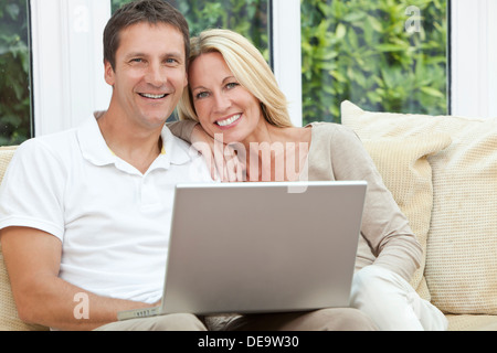 Successful, happy middle aged man and woman couple in their forties, sitting together at home on a sofa using laptop computer Stock Photo