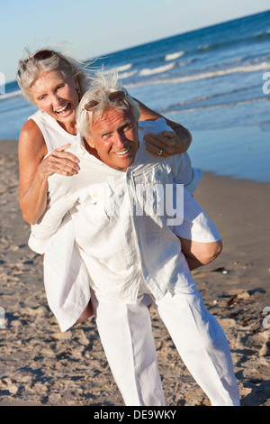 Happy senior man and woman couple playing piggy back and having fun on a deserted tropical beach Stock Photo