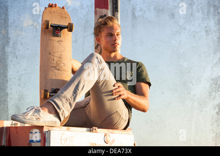 A young skateboarder rests on a utility box at the beach. Stock Photo