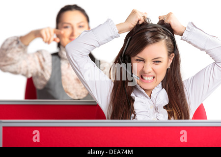 Angry frustrated call center female agent screaming and pulling her hair in rage with female colleague pointing at her. Stock Photo