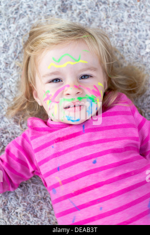 Child with paint on face lying on the floor Stock Photo