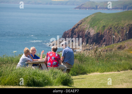 Caldey Island group of four friends middle aged 50s sitting around table chatting coast and sea behind Pembrokeshire wales UK Stock Photo