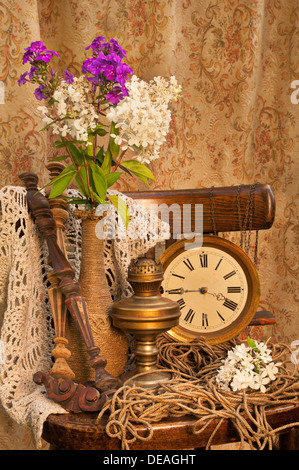 still life with phlox bouquet in a vintage vase on the old chair with antique clock and oil lamp Stock Photo