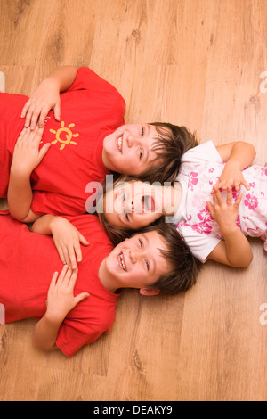 Girl, 4 years, and boys, 6 and 11 years, lying on the floor, laughing Stock Photo