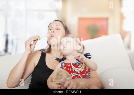 Mother and daughter sitting on the couch and blowing bubbles in the living room Stock Photo
