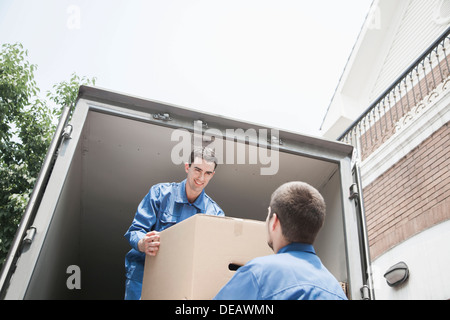 Movers unloading a moving van, passing a cardboard box Stock Photo