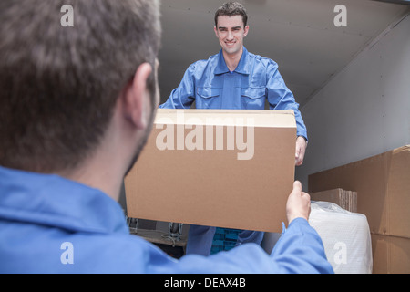 Movers unloading a moving van, passing a cardboard box Stock Photo