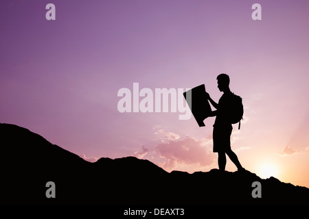 Silhouette of young man looking at a map in nature while hiking Stock Photo