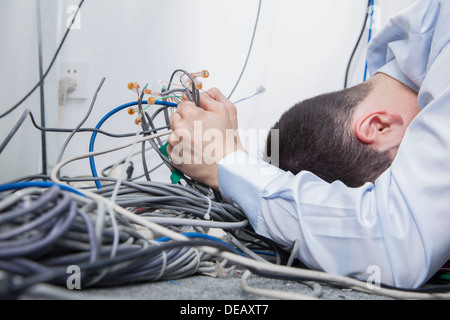 Frustrated man lying down trying to figure out and sort  computer cables Stock Photo