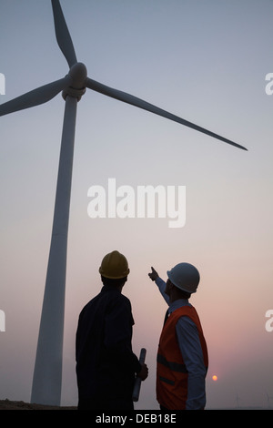 Two young male engineers standing beside a wind turbine at sunset, pointing up Stock Photo