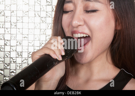 Close-up of young woman singing into a microphone at karaoke Stock Photo
