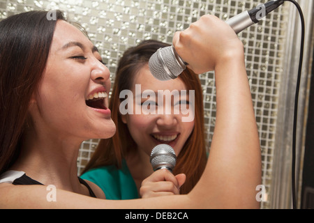 Two young female friends singing into a microphone at karaoke Stock Photo
