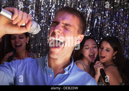 Young man singing into a microphone at karaoke, friends singing in the background Stock Photo