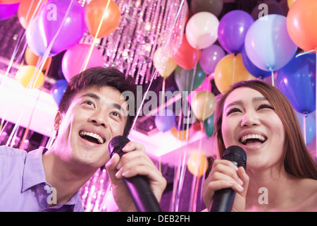 Two friends holding microphones and singing together at karaoke, balloons in the background