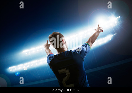 Soccer player with arms raised cheering, stadium at night time Stock Photo