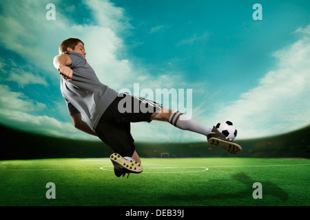 Soccer player kicking the soccer ball in mid air, in the stadium with the sky Stock Photo