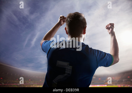 Soccer player with arms raised cheering, stadium with sky and clouds Stock Photo