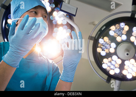 Low angle view of surgeon holding gloved hands up with surgical lights behind him Stock Photo
