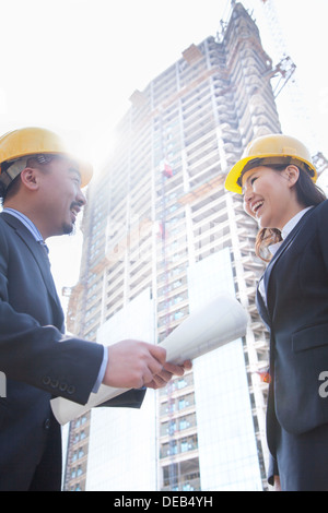 Two architects smiling at a construction site holding blueprint Stock Photo