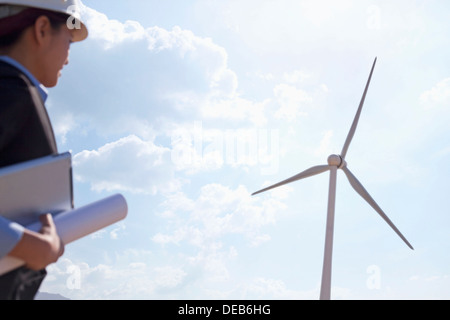 Young female engineer holding blueprints and checking wind turbines on site Stock Photo