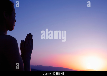 Serene young woman with hands together in prayer pose  in the desert in China, silhouette, sun setting Stock Photo