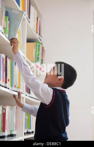 Schoolboy reaching for book off bookshelf Stock Photo