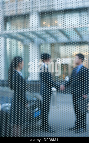 Two businessmen shaking hands outside behind a glass wall Stock Photo