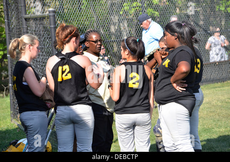 coach discusses strategy with her team at a high school softball game Stock Photo