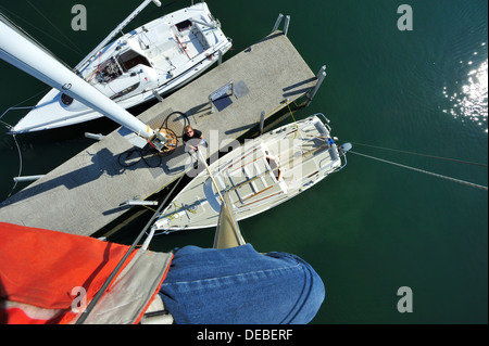 At the masthead. A sailor at the top of his mast for maintenance, photographs the yacht below. Stock Photo