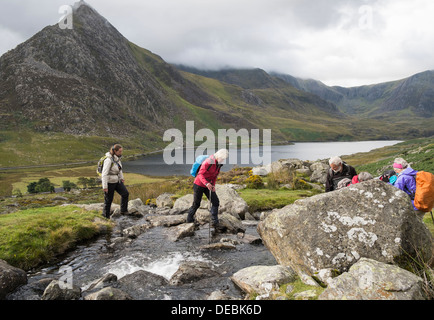 Walkers crossing a mountain stream stepping on stones In mountains of Snowdonia National Park, Ogwen Valley, North Wales, UK Stock Photo